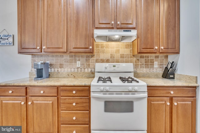 kitchen featuring under cabinet range hood, decorative backsplash, light stone countertops, and white range with gas stovetop