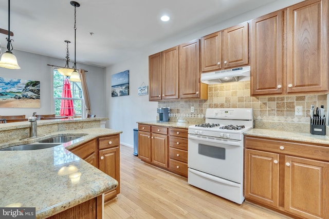 kitchen with under cabinet range hood, white gas range, decorative backsplash, light wood-style floors, and a sink