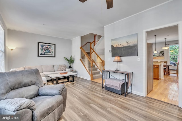 living room featuring stairs, light wood-style floors, baseboards, and a ceiling fan