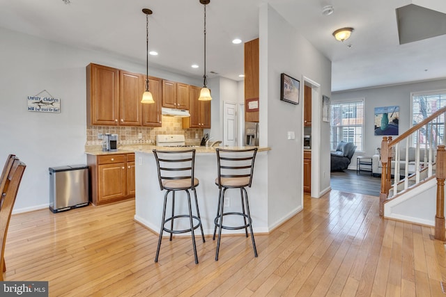 kitchen featuring backsplash, decorative light fixtures, a breakfast bar area, light wood-style flooring, and stainless steel fridge