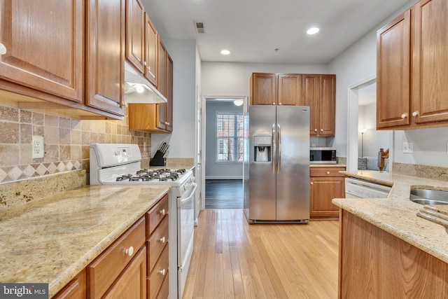 kitchen featuring under cabinet range hood, appliances with stainless steel finishes, light wood-style floors, and light stone countertops