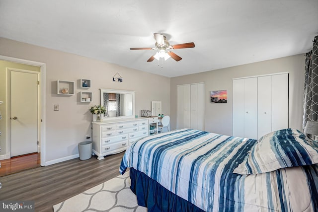 bedroom featuring two closets, a ceiling fan, baseboards, and wood finished floors