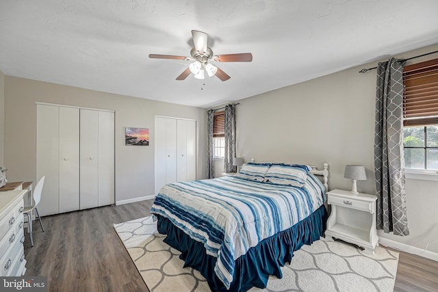 bedroom featuring ceiling fan, two closets, baseboards, and wood finished floors