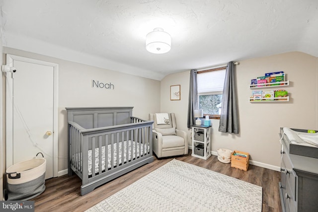 bedroom featuring baseboards, a crib, lofted ceiling, and wood finished floors