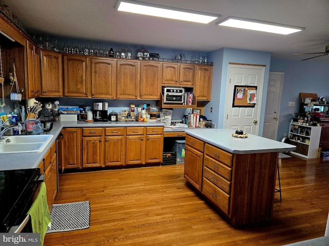 kitchen featuring a sink, light countertops, a kitchen bar, light wood-style floors, and brown cabinetry