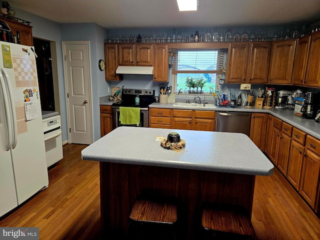 kitchen featuring under cabinet range hood, wood finished floors, a sink, light countertops, and stainless steel appliances
