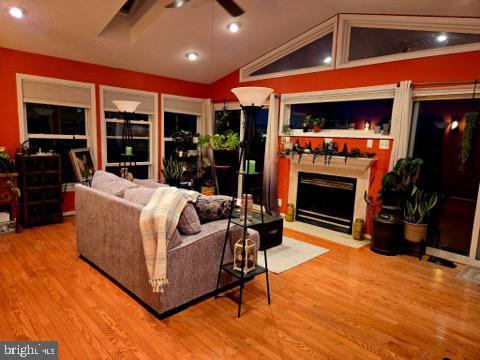 living room featuring a ceiling fan, vaulted ceiling, a fireplace with flush hearth, and wood finished floors