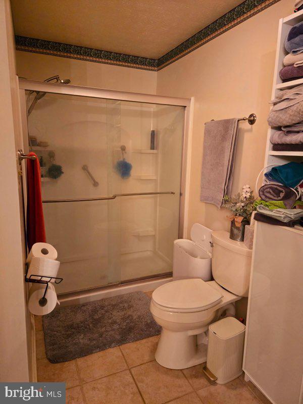 bathroom featuring tile patterned flooring, a stall shower, and toilet