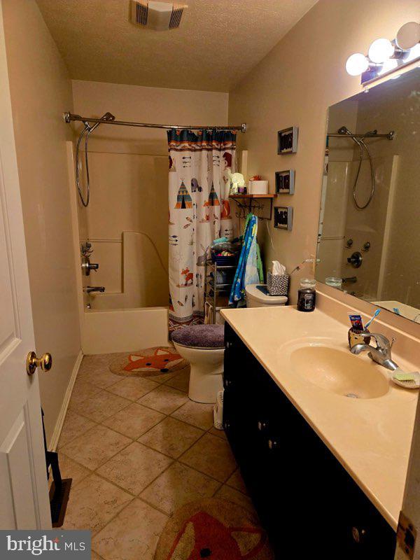 bathroom featuring visible vents, shower / bath combination with curtain, a textured ceiling, tile patterned flooring, and vanity