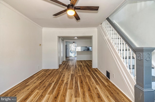 unfurnished living room with visible vents, stairway, ornamental molding, wood finished floors, and a ceiling fan