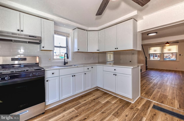 kitchen featuring stainless steel gas stove, a ceiling fan, under cabinet range hood, a sink, and white cabinets