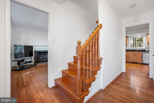 staircase featuring visible vents, a fireplace with raised hearth, and wood finished floors