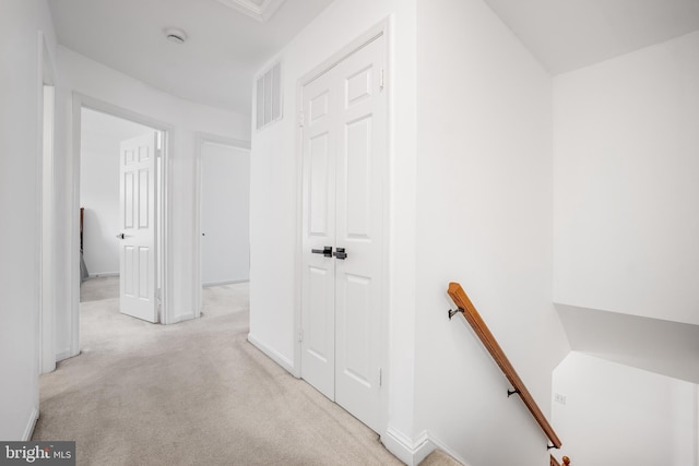 hall with an upstairs landing, visible vents, light carpet, and baseboards