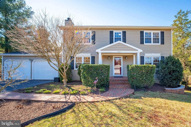 colonial home featuring a garage, driveway, a front lawn, and a chimney