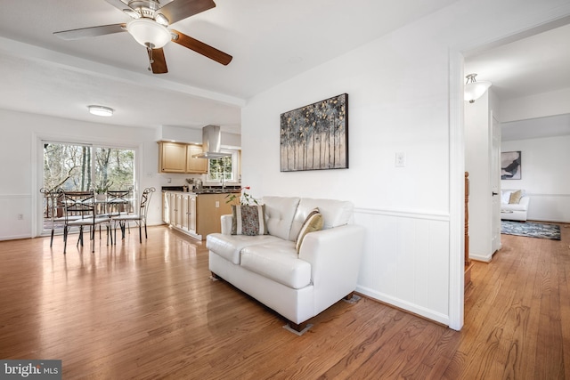 living area with a ceiling fan, light wood-type flooring, and wainscoting