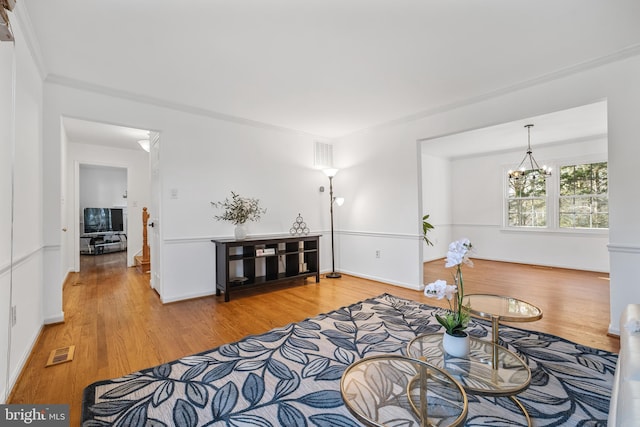 living area featuring visible vents, an inviting chandelier, ornamental molding, and light wood finished floors