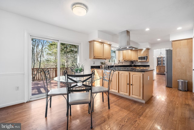 kitchen featuring dark countertops, light brown cabinetry, appliances with stainless steel finishes, light wood-style floors, and island range hood