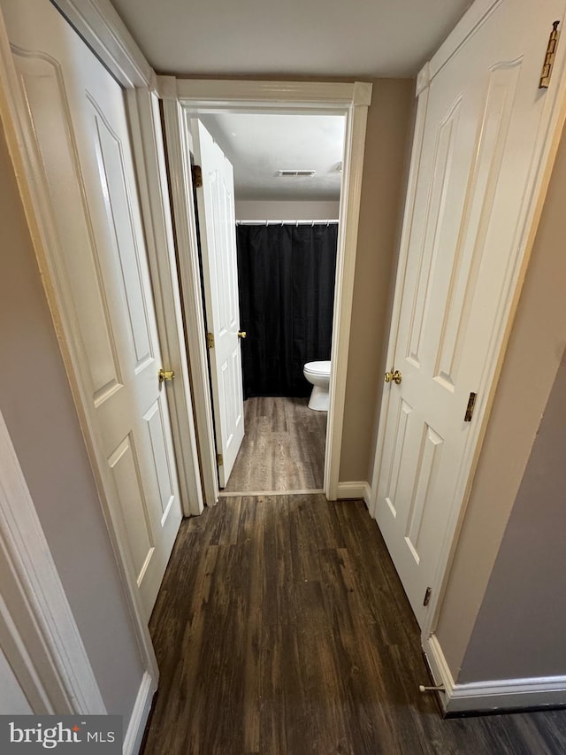 hallway with visible vents, baseboards, and dark wood-type flooring