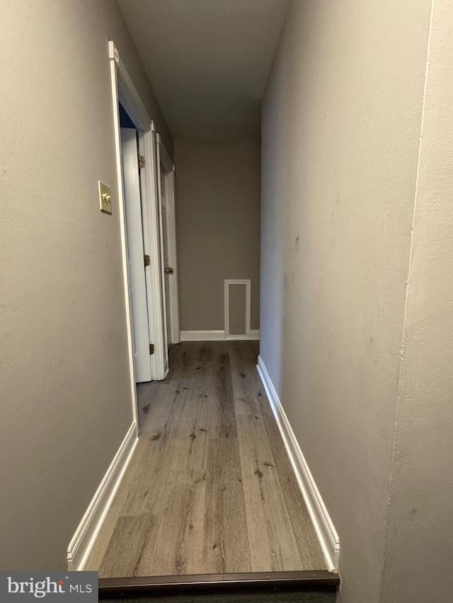 hallway featuring visible vents, wood finished floors, and baseboards