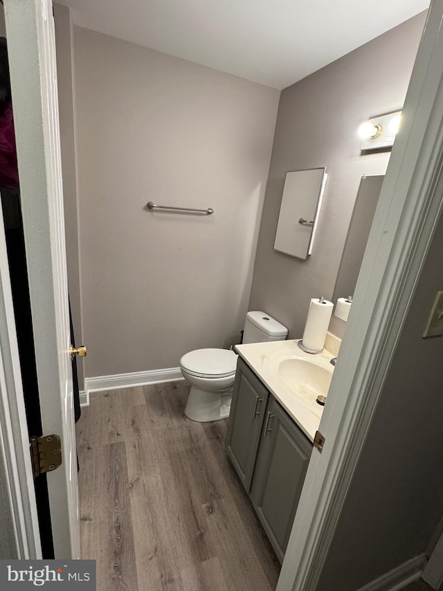 half bath with baseboards, toilet, wood finished floors, and vanity