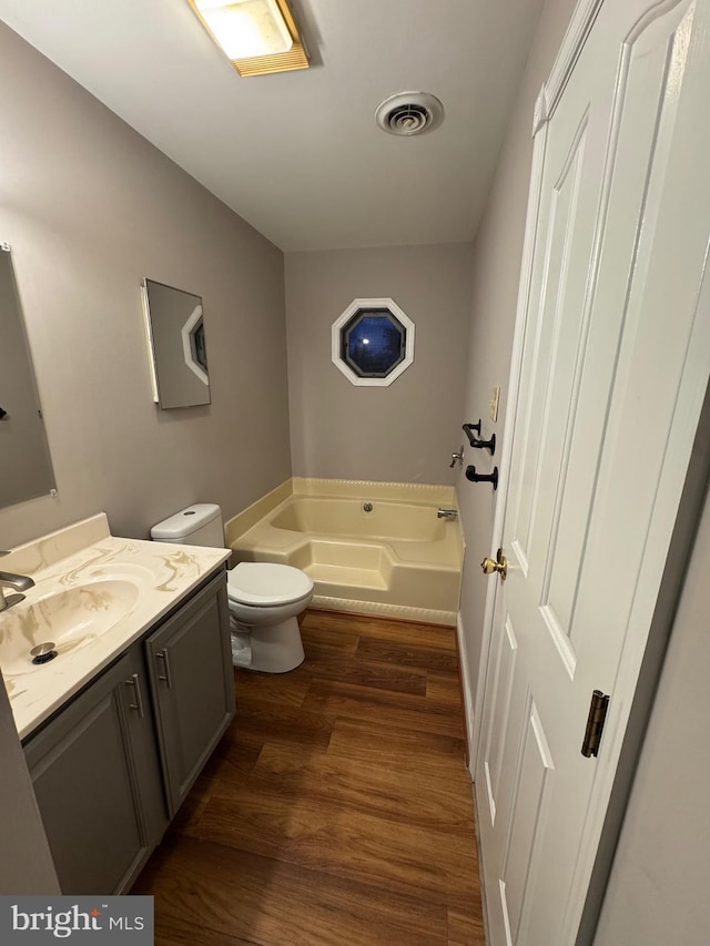 bathroom featuring visible vents, toilet, wood finished floors, a bath, and vanity