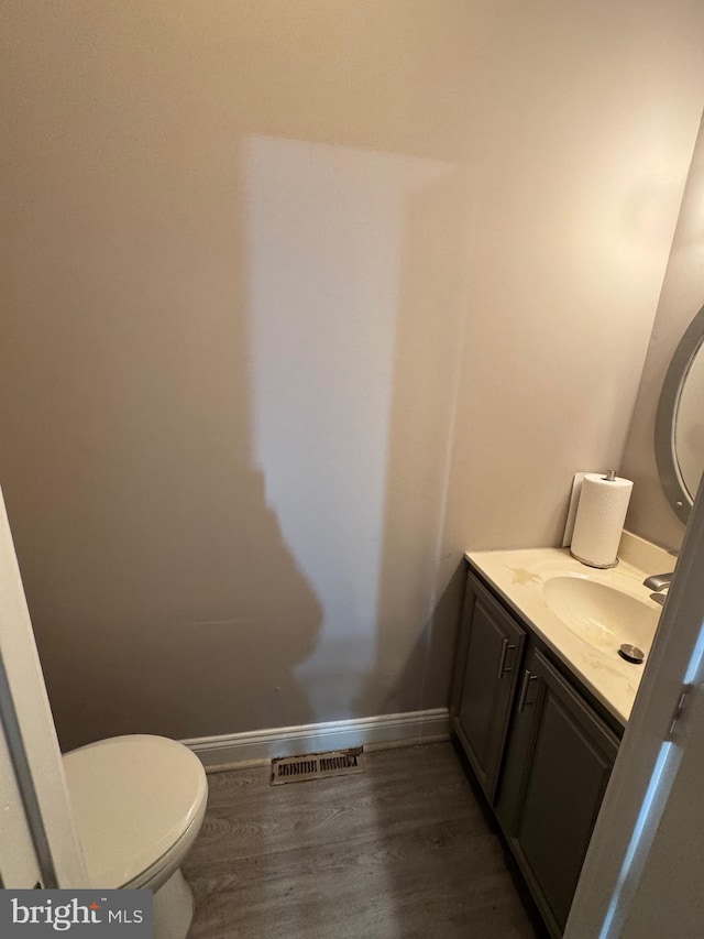 half bath featuring visible vents, baseboards, toilet, wood finished floors, and vanity