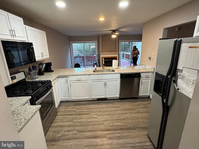 kitchen with a sink, a peninsula, white cabinets, stainless steel appliances, and dark wood-style flooring