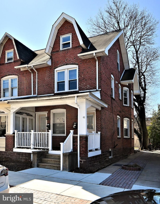 view of front facade featuring covered porch, brick siding, and a gambrel roof