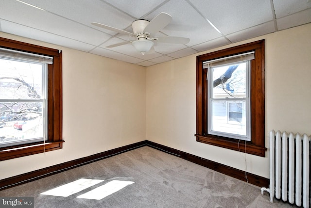 carpeted spare room featuring ceiling fan, radiator, a paneled ceiling, and baseboards