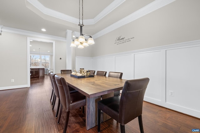 dining space with a wainscoted wall, ornamental molding, dark wood-style floors, a decorative wall, and a raised ceiling