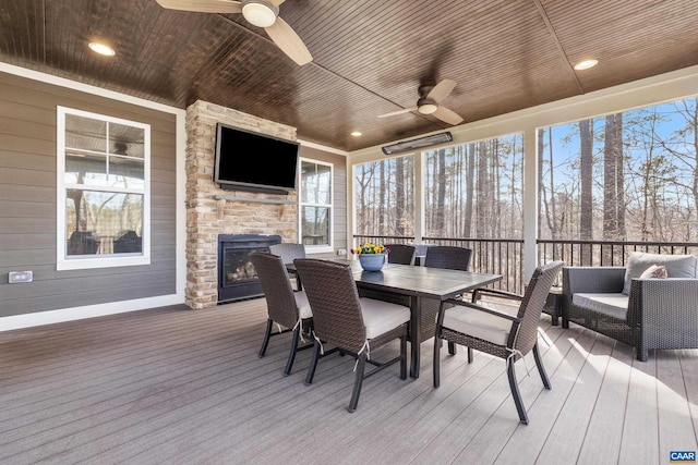 deck featuring exterior fireplace, outdoor dining area, and a ceiling fan