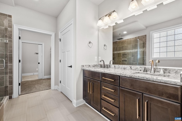 full bath with double vanity, a shower stall, baseboards, and a sink