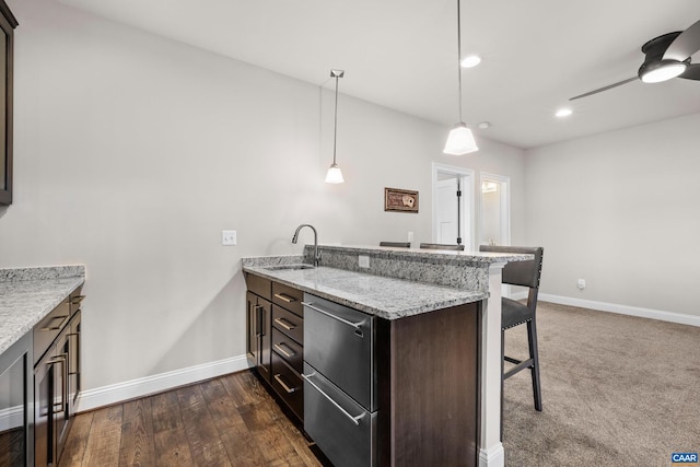 kitchen with a breakfast bar, a sink, a peninsula, baseboards, and ceiling fan