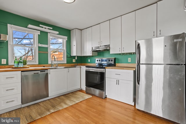 kitchen with a sink, white cabinets, light wood-style floors, under cabinet range hood, and appliances with stainless steel finishes