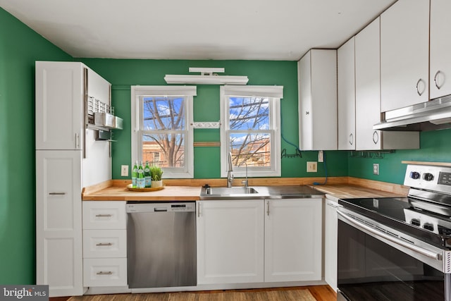 kitchen with a sink, stainless steel appliances, under cabinet range hood, wood counters, and white cabinetry