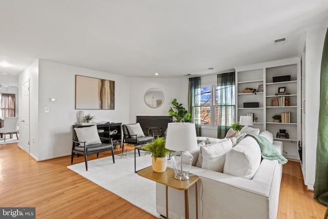 living area featuring a glass covered fireplace, baseboards, light wood-type flooring, and visible vents