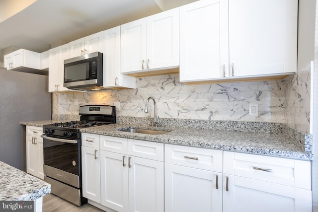 kitchen with light stone countertops, a sink, white cabinets, appliances with stainless steel finishes, and tasteful backsplash