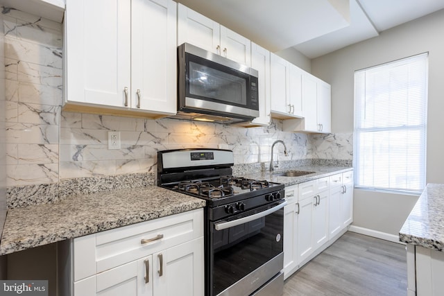 kitchen featuring a sink, light stone counters, backsplash, stainless steel appliances, and white cabinets