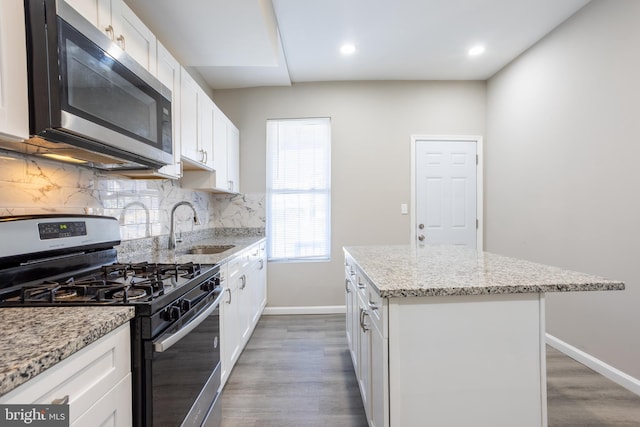 kitchen featuring a sink, a center island, appliances with stainless steel finishes, decorative backsplash, and baseboards