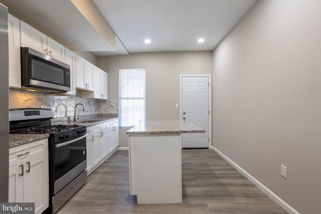 kitchen with light stone counters, a kitchen island, stainless steel appliances, white cabinets, and backsplash