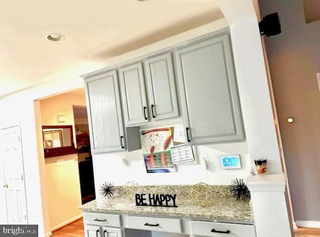 kitchen featuring light stone counters, gray cabinetry, and baseboards