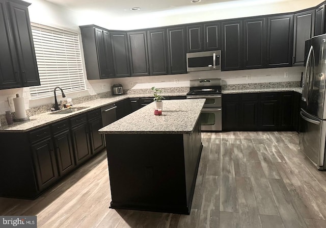 kitchen featuring dark cabinets, stainless steel appliances, light wood-type flooring, and a sink