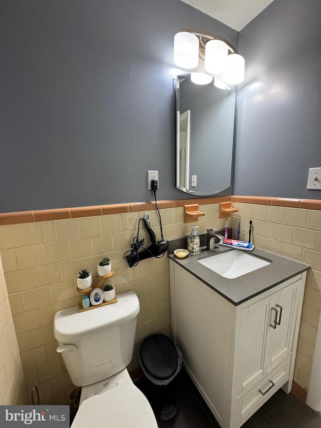 half bath with tile walls, a wainscoted wall, toilet, tile patterned floors, and vanity