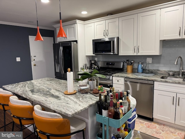 kitchen featuring ornamental molding, decorative backsplash, a sink, appliances with stainless steel finishes, and a kitchen bar