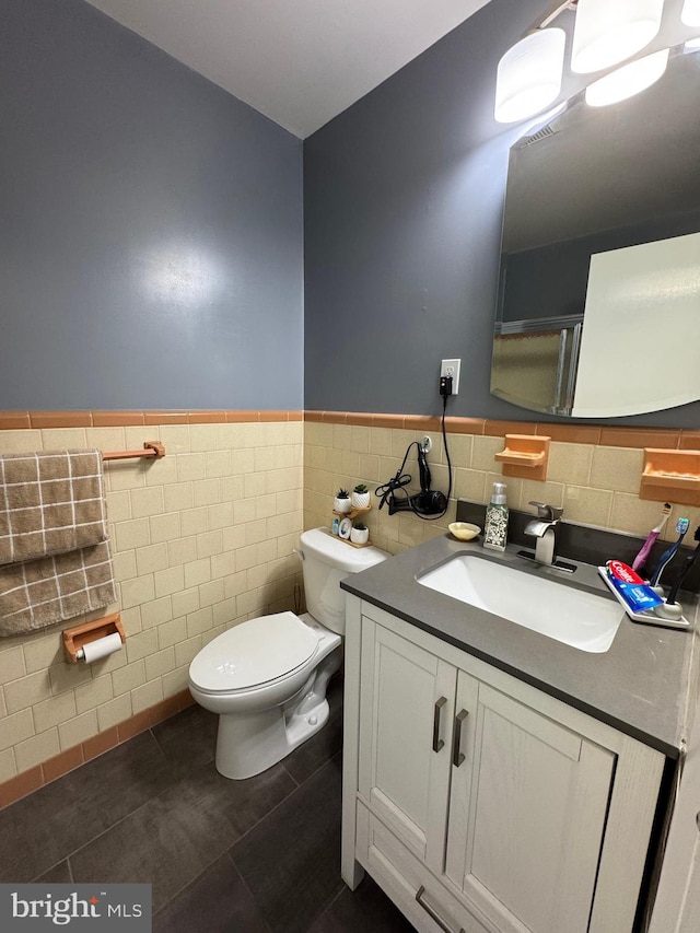 bathroom featuring a wainscoted wall, toilet, tile walls, tile patterned flooring, and vanity