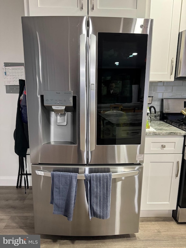 details featuring light stone counters, stainless steel appliances, white cabinets, light wood-type flooring, and backsplash