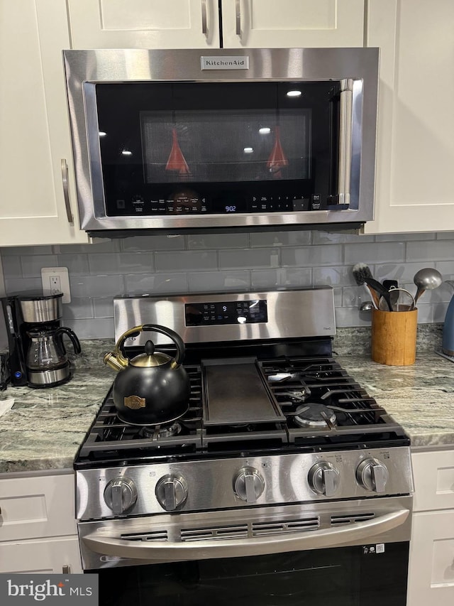 interior details with white cabinets, light stone counters, backsplash, and stainless steel appliances