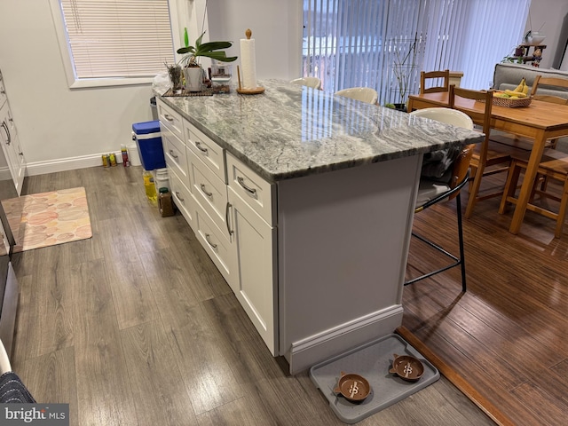 kitchen featuring a kitchen bar, a kitchen island, white cabinets, light stone countertops, and dark wood-style flooring