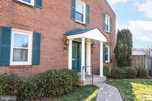 view of exterior entry with brick siding and fence