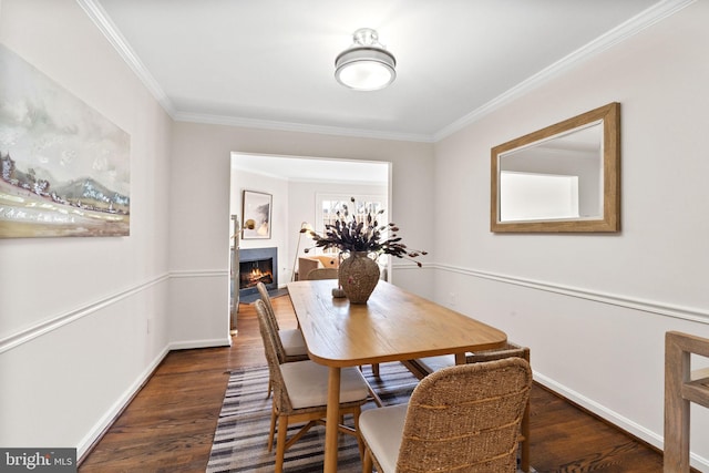 dining area featuring wood finished floors, baseboards, a warm lit fireplace, and ornamental molding